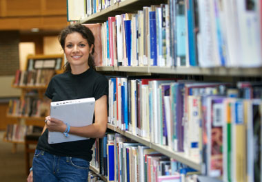 female student leaning against library shelf smiling